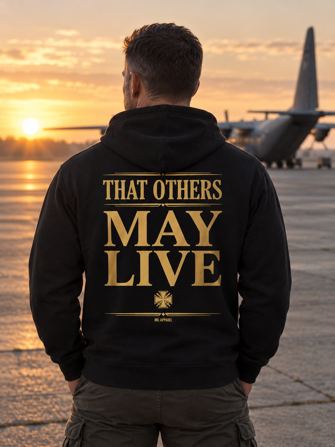 Man wearing the black Guardian Angel hoodie on a flight line at sunrise, showing the THAT OTHERS MAY LIVE back print